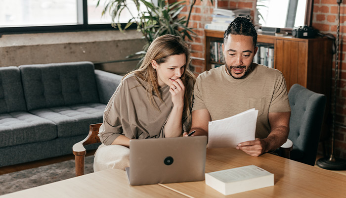 Diverse couple sitting at a table with their laptop and documents discussing their finances.