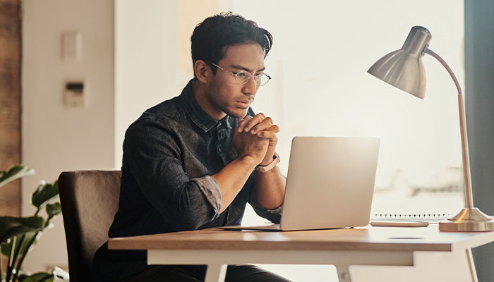 Asian business man looking at this computer with a concerned look on his face.