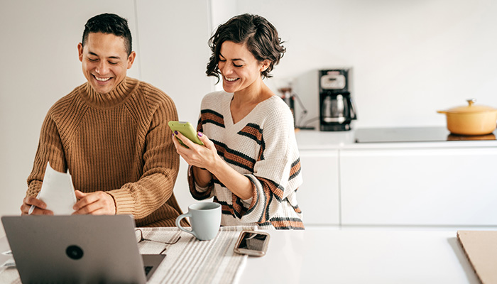 Hispanic couple in kitchen at computer with phone and paperwork